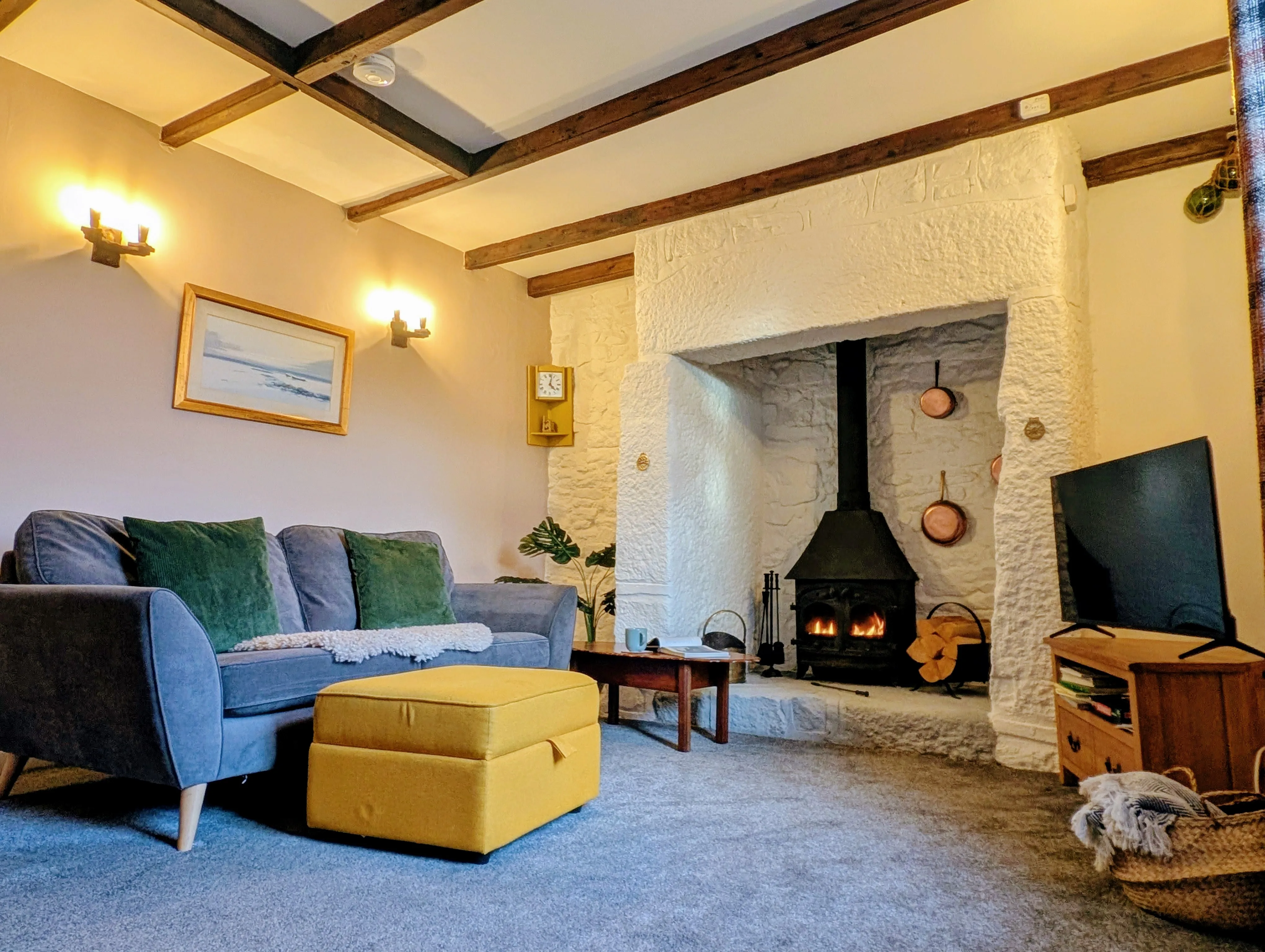 Little Avalon lounge. Sofa with cushions, wood burner in the original granite fireplace, exposed beams.