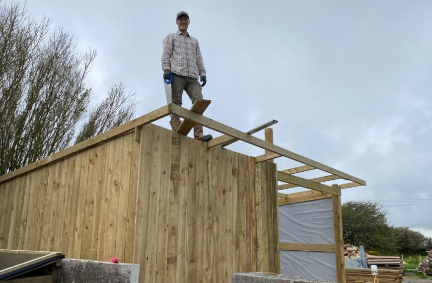 Rich standing on the framework of a wooden structure under construction.