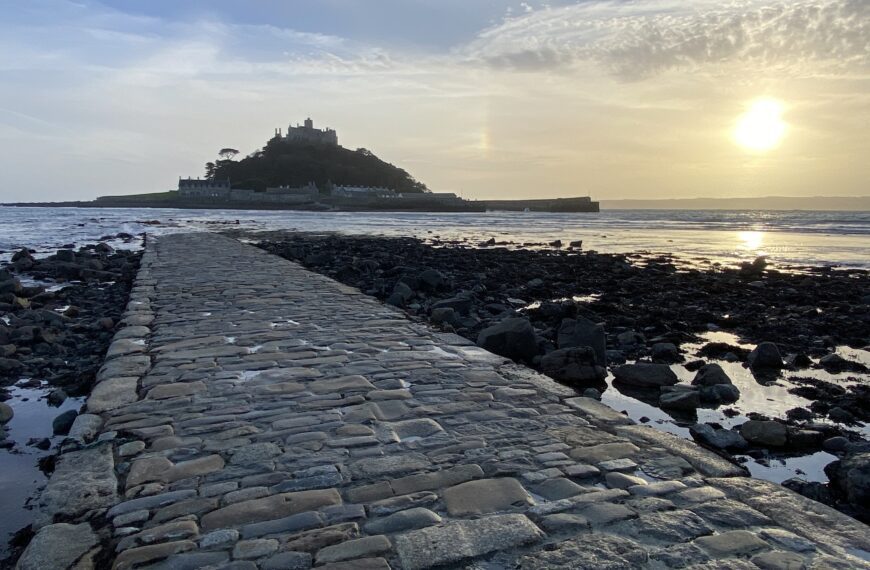 Cobblestone causeway leading to St Michael’s Mount in Cornwall at sunset, with the tide out and golden light on the water.
