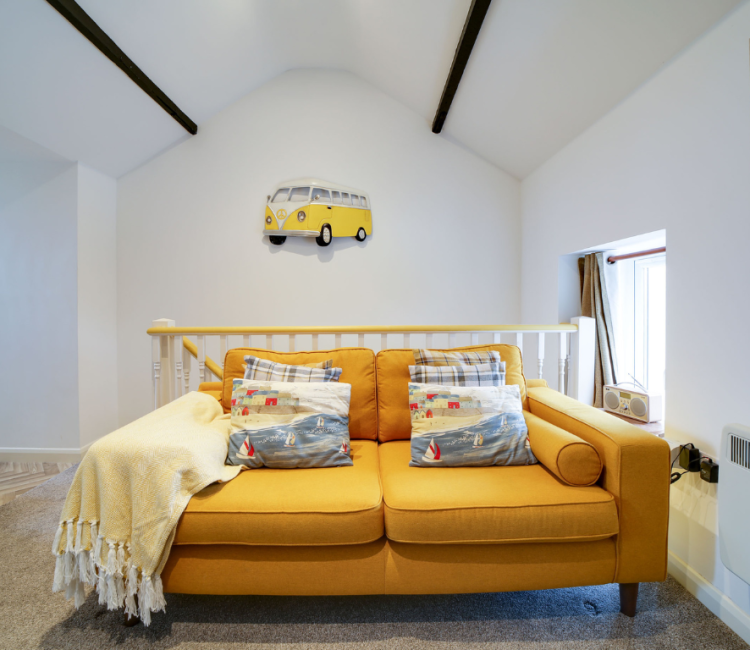 Mustard yellow sofa in The Pigsty’s living area, decorated with nautical-themed cushions and a soft blanket.